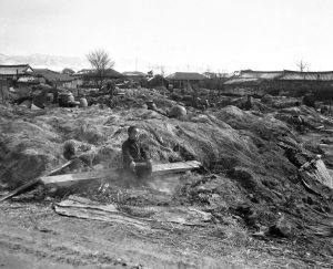 Korean boy sits in smoldering ruins of his home, allied troops burned dwellings which might provide shelter for North Korean troops, by Jim Pringle, 1951 