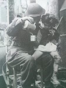 British soldier brews soup for a wounded young girl in Caen, 1944.
